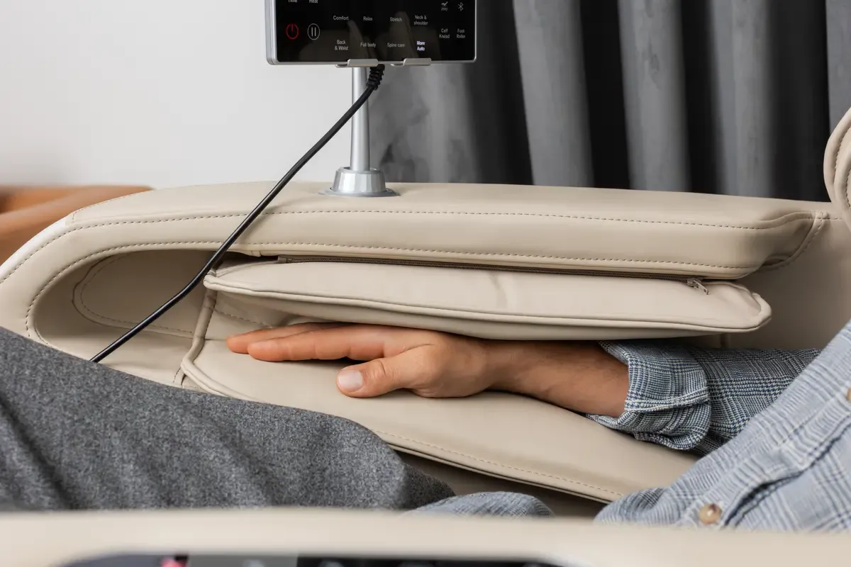 A hand resting in the cushioned armrest of a beige massage chair